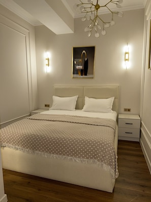 Quarto com cama grande, duas mesas de cabeceira, um criado-mudo, um candelabro e uma obra de arte emoldurada na parede.