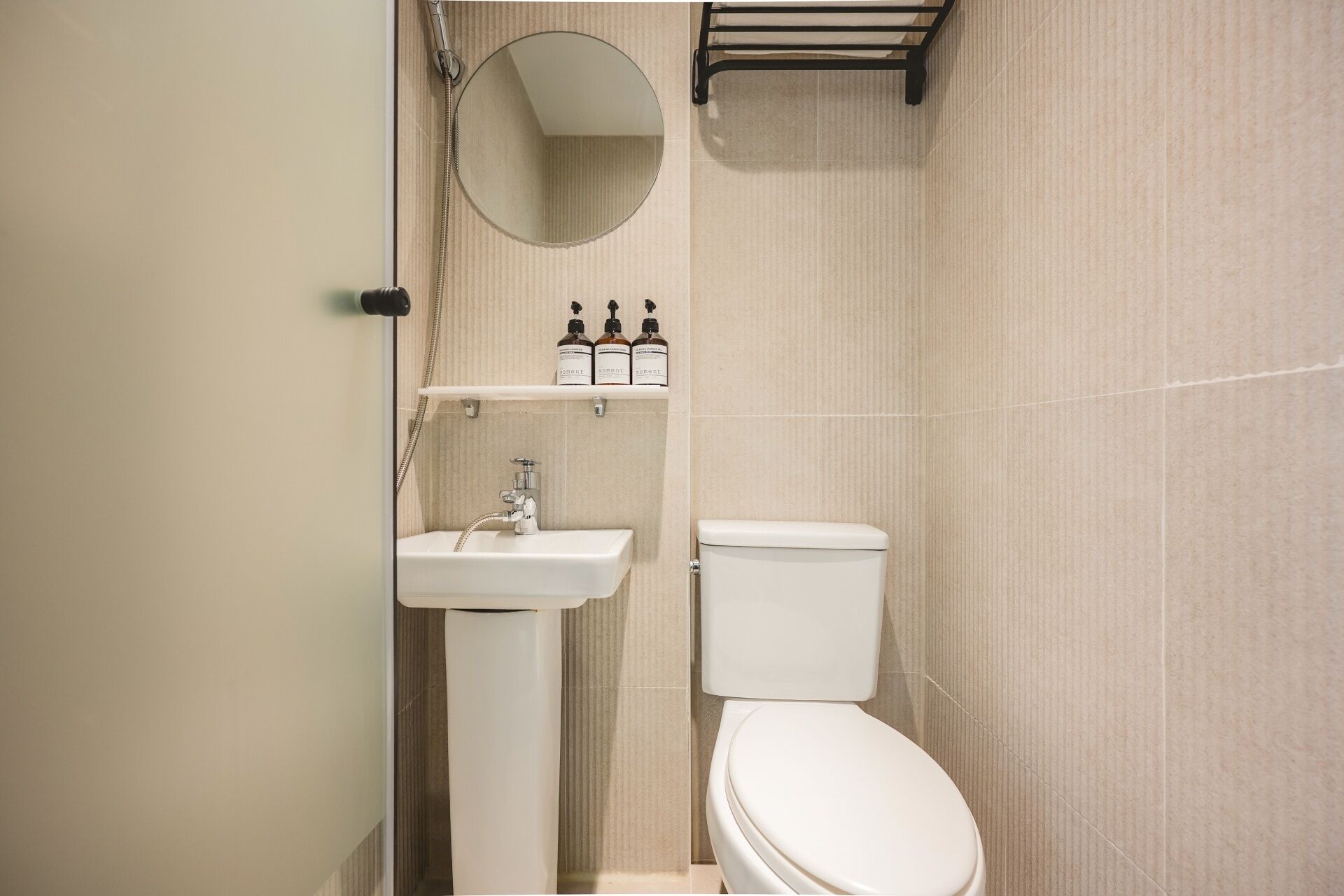 A bathroom with a sink, toilet, mirror, and shelf with toiletries.
