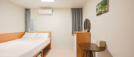 Habitación de hotel con cama, escritorio, silla, mesita, espejo, aire acondicionado y ventana con cortinas.
