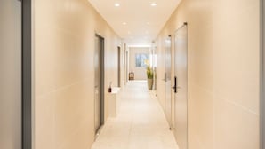 A corridor with beige walls and a tiled floor, leading to a room with a window and a potted plant. - Stay Log in Sinchon Hongdae (Seoul)