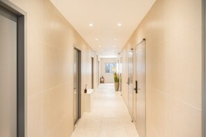 Passadís amb parets beix i un paviment de rajoles, que condueix a una habitació amb finestra i una planta en test.