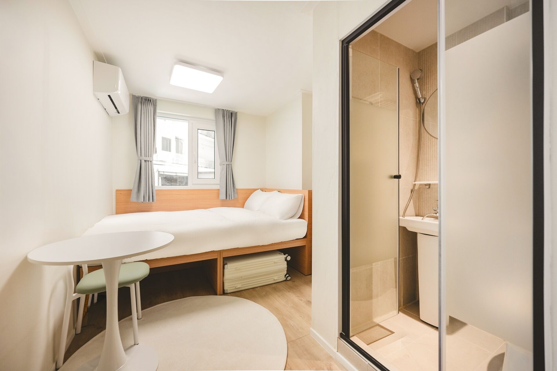 Une chambre d’hôtel comprenant un lit, une petite table, une chaise, un radiateur et une cabine de douche en verre.
