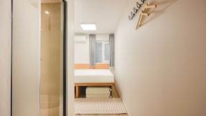 A narrow hallway leading to a bedroom with a bed, a window with curtains, and a wall-mounted light fixture. - Stay Log in Sinchon Hongdae (Seoul)