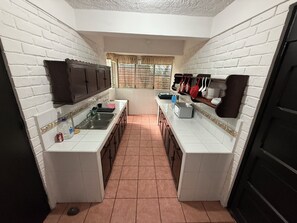 A compact kitchen with white tiled walls, a central island, and a window with blinds. - Loma Linda Essenz. 152B (San Salvador)