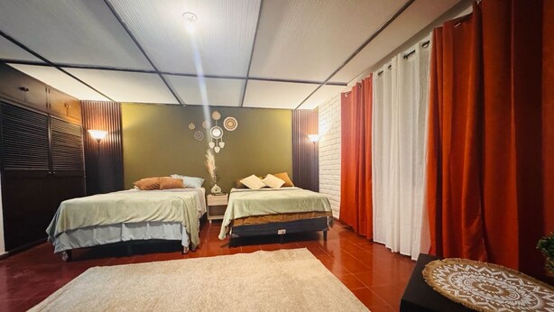 A room with two beds, a large rug, a wall with a circular design, and a window with curtains. - Loma Linda Essenz. 152B (San Salvador)