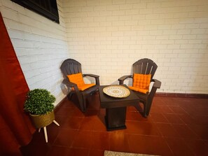 A corner seating area with two chairs and a table, a small potted plant, and a white brick wall. - Loma Linda Essenz. 152B (San Salvador)