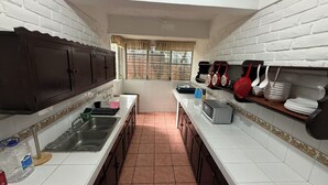A kitchen with white tiled walls, dark wooden cabinets, a stainless steel sink, and a window with curtains. - Loma Linda Essenz. 152B (San Salvador)