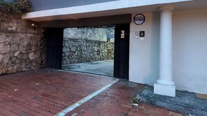 A building entrance with a stone wall, a black gate, and a sign indicating security services. - Loma Linda Essenz. 152B (San Salvador)