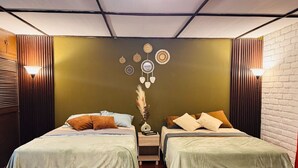 A room with two beds, a wall with circular decorations, a vase with dried plants, and two wall-mounted lamps. - Loma Linda Essenz. 152B (San Salvador)
