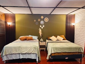 A room with two beds, a wall with circular decorations, a vase with dried plants, and two wall-mounted lamps. - Loma Linda Essenz. 152B (San Salvador)
