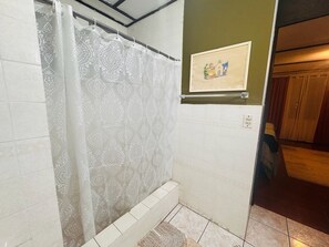 A bathroom with a shower curtain, tiled walls, a framed picture on the wall, and a visible door leading to another room. - Loma Linda Essenz. 152B (San Salvador)