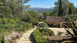 Una casa di campagna con tetto in tegole, immersa nel verde e con un vialetto sterrato che vi conduce.