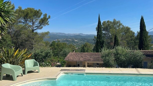 Una piscina con due sedie, un edificio con tetto in tegole e alberi sullo sfondo.