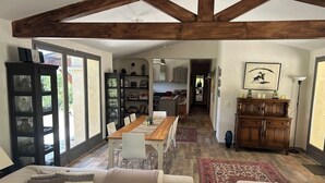 Un ampio soggiorno con soffitto alto, una zona pranzo e una cucina visibile tramite un'apertura.