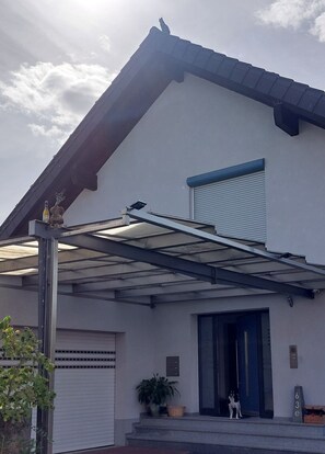 Ett modernt hus i två våningar med en täckt uteplats, ett garage och en hund som står vid entrén.