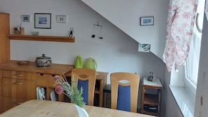 A kitchen with wooden cabinets, a dining table with chairs, a window with a floral curtain, and a shelf with framed pictures and a scale. - Experience the Palatinate, enjoy vineyards with your pet (Gerolsheim)