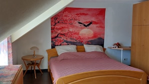 A bedroom with a bed, a round wooden table, a small shelf, and a large tapestry depicting cherry blossoms and a bird. - Experience the Palatinate, enjoy vineyards with your pet (Gerolsheim)