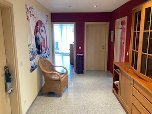 Un couloir avec un fauteuil en osier, une armoire et une porte donnant sur un espace extérieur.