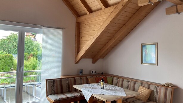 A room with a wooden ceiling, a dining table with a white tablecloth, a bench seating area, and a large window with blinds. - Experience the Palatinate, enjoy vineyards with your pet (Gerolsheim)