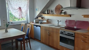 A kitchen with wooden cabinets, a dishwasher, an oven, a sink, and a window with curtains. - Experience the Palatinate, enjoy vineyards with your pet (Gerolsheim)