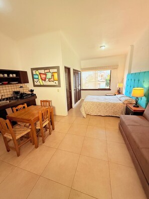 A compact room with a bed, a sofa, a dining table with chairs, a kitchen area, and a window with a view. - 2 minutes walk to the boardwalk and 4 to the beach (Puerto Vallarta)