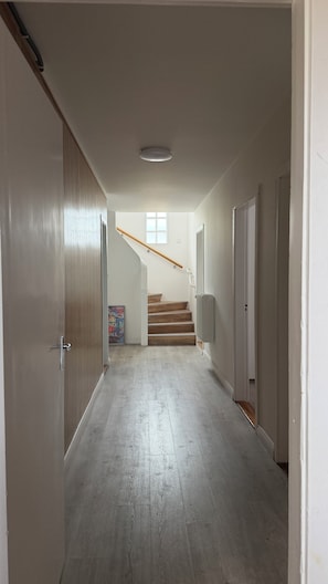 Un couloir avec un escalier en bois, des murs blancs et un luminaire au plafond.