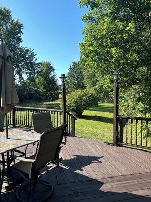 A wooden deck with outdoor furniture, a railing, and a view of a green lawn and trees. - Peaceful Tree-Lined Retreat Near Cleveland (North Olmsted)