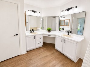 A bathroom with two sinks, white cabinetry, a wooden floor, and a door. - Peaceful Tree-Lined Retreat Near Cleveland (North Olmsted)