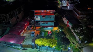 A multi-story building with a red roof, a visible entrance, and a small garden area with a tree. - Flyo Stayo - Naukuchiatal (Nainital)