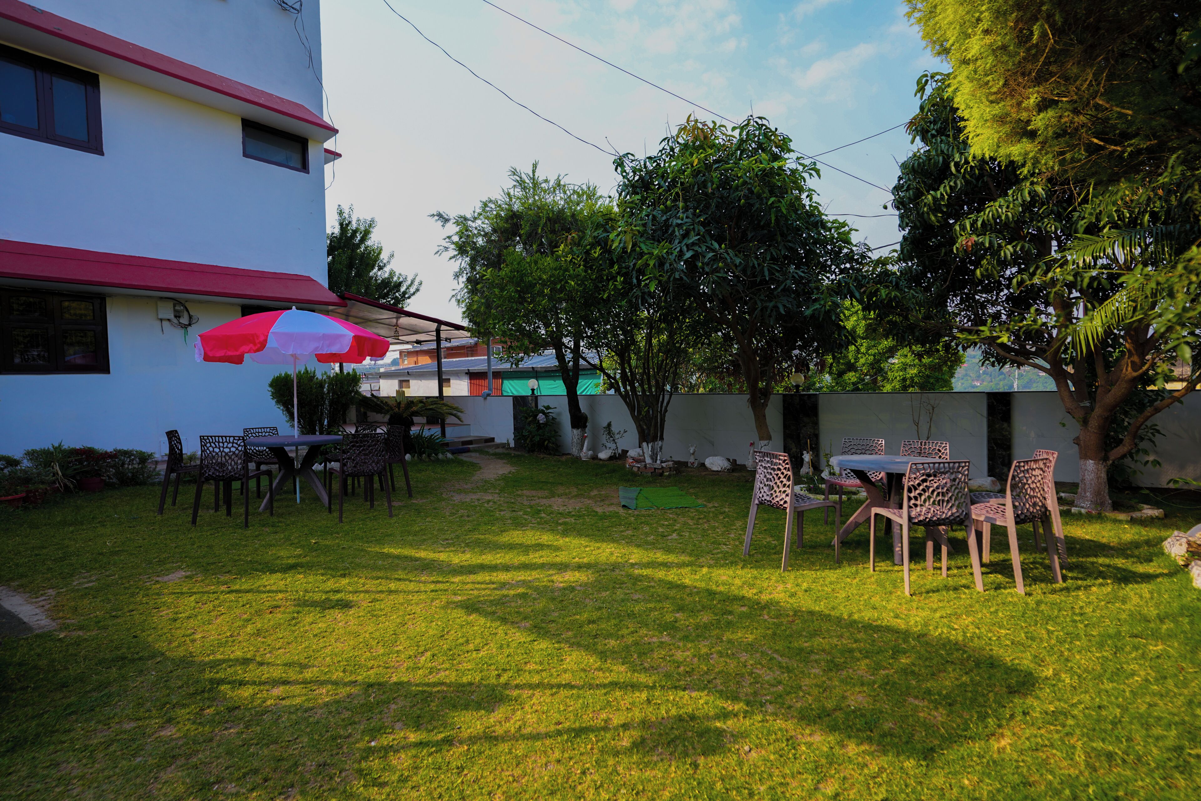 An outdoor seating area with tables and chairs, a red and white umbrella, and a building in the background.