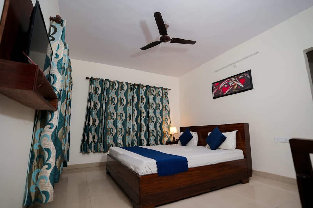 A bedroom with a bed, curtains, a ceiling fan, a wall-mounted TV, and a painting.