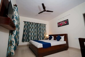 A bedroom with a bed, curtains, a ceiling fan, a wall-mounted TV, and a painting.