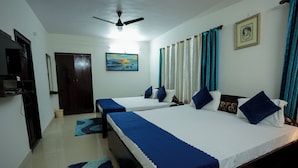 Habitación de hotel con dos camas, ventilador de techo, televisión, un cuadro y cortinas.