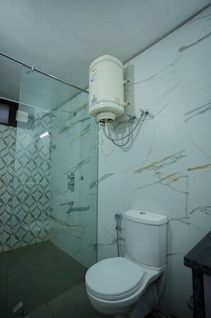 A bathroom with a toilet, a glass shower enclosure, and a marble-patterned wall. - Flyo Stayo - Naukuchiatal (Nainital)