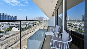 A balcony with a city view, white chairs, and a glass table. - Bloomfields 1BR in Azizi Riviera 3  (Dubai)