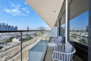 A balcony with a city view, white chairs, and a glass table. - Bloomfields 1BR in Azizi Riviera 3  (Dubai)