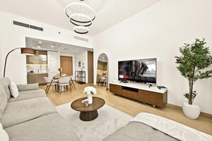 A modern living room with a sofa, coffee table, TV, and a dining area. - Bloomfields 1BR in Azizi Riviera 3  (Dubai)