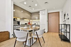 A modern kitchen with a dining table and chairs, a washing machine, and a wooden door. - Bloomfields 1BR in Azizi Riviera 3  (Dubai)