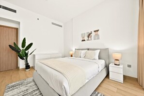 A modern bedroom with a bed, bedside tables, a plant, and wall art. - Bloomfields 1BR in Azizi Riviera 3  (Dubai)