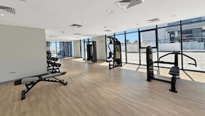 A modern gym with various exercise equipment, large windows, and a wooden floor. - Bloomfields 1BR in Azizi Riviera 3  (Dubai)