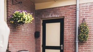 A brick wall, a door, two chairs, and hanging flower baskets. - Cosy studio in Hoorn perfect for a relaxing getaway (Hoorn)