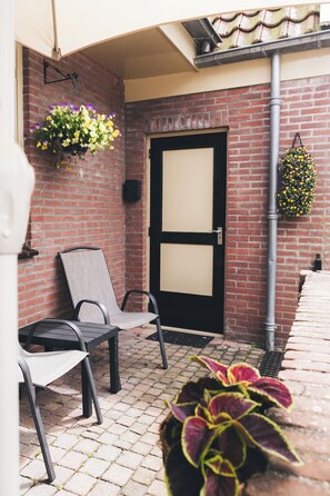 A brick wall, a door, two chairs, and hanging flower baskets. - Cosy studio in Hoorn perfect for a relaxing getaway (Hoorn)
