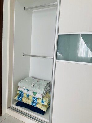 A walk-in closet with a metal rod for hanging clothes, a glass door, and a shelf with folded clothes.