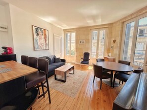 A modern living room with a sofa, coffee table, and dining table. There are two doors leading to a balcony. - Vrbo Property (Bordeaux)
