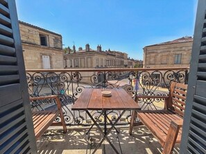 An outdoor balcony with a wooden table and chairs, a wrought iron railing, and a view of historic buildings. - Vrbo Property (Bordeaux)
