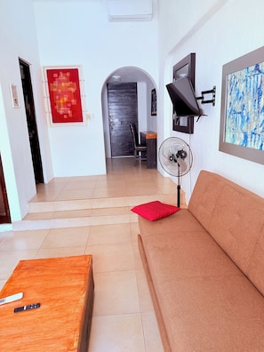 A living room with a sofa, a wooden coffee table, a red cushion, a fan, and a TV on the wall. - 2 minutes walk to the boardwalk and 4 to the beach (Puerto Vallarta)