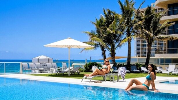 A pool area with lounge chairs, palm trees, and a clear view of the ocean. - Surf & Sunrise Beachfront Hideaway by Inn Paradise (Surfers Paradise)