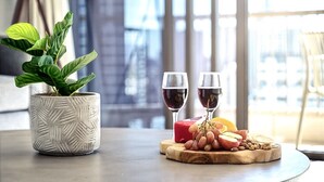 A table with a potted plant, two glasses of red wine, and a wooden board with fruits and cheese. - Surf & Sunrise Beachfront Hideaway by Inn Paradise (Surfers Paradise)