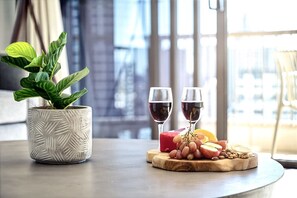 A table with a potted plant, two glasses of red wine, and a wooden board with fruits and cheese. - Surf & Sunrise Beachfront Hideaway by Inn Paradise (Surfers Paradise)