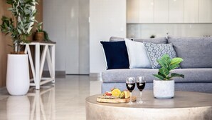 A modern living room with a grey sofa, a round coffee table with snacks and drinks, and a potted plant. - Surf & Sunrise Beachfront Hideaway by Inn Paradise (Surfers Paradise)